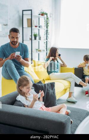 father with two children using smartphones while mother talking on smartphone at home Stock Photo