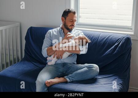 Middle age Caucasian father feeding newborn baby from bottle milk. Man parent holding rocking child on his hands. Authentic lifestyle candid real mome Stock Photo