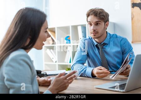 handsome travel agent pointing with pen at map while talking to smiling woman Stock Photo