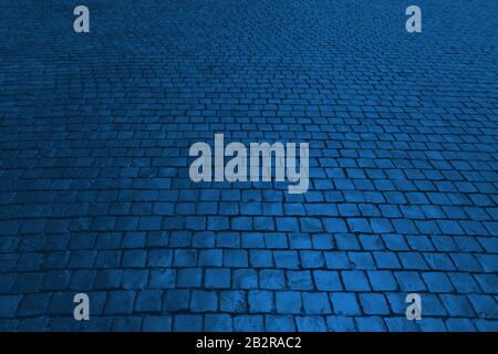 Old cobblestone pavement in perspective in color Pantone classic blue 2020. Color of the year. Abstract background. Monochrome photo. Stock Photo