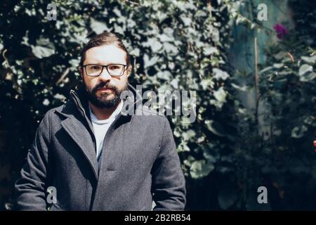 Bearded man in black jacket wearing eyeglasses with a blurred background Stock Photo
