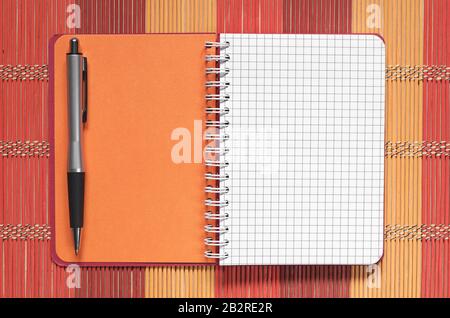 Opened notebook with pen on a colorful bamboo napkin, top view Stock Photo