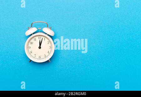 White vintage alarm clock on light blue color background Stock Photo