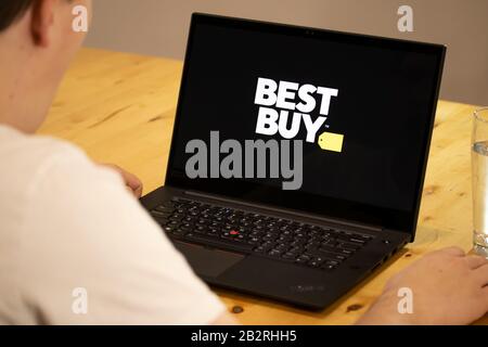 Man sitting at a desk using a laptop with the Best Buy logo on-screen. Stock Photo