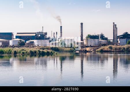 Smoke billowing from a factory smokestack reflected on the banks of the River Nile in Egypt Stock Photo