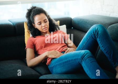 Young Black Woman With Menstrual Pain Lying On Sofa Stock Photo