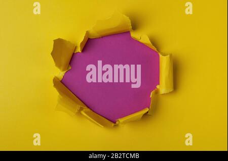 Bright yellow torn paper with pink purple hole. Abstract minimalistic background. Stock Photo
