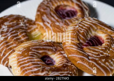 Danish pastry close up on a plate. Freshly iced sweet buns for breakfast and dessert. Homemade Danish pastry treats. Delicious baked goods. Stock Photo