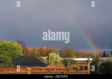 Rainbow in a grey sky over backyards & gardens during autumn Stock Photo