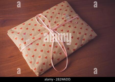Gift in paper packaging with a pattern of red hearts on the table. Stock Photo