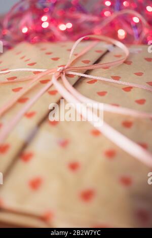 Gift in paper packaging, ribbon bow and pink lights on background Stock Photo