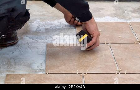 A contractor installing and measuring ceramic tiles and adding spacers between tiles on a concrete floor. Stock Photo