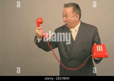 Portrait of mature Asian businessman with old telephone Stock Photo