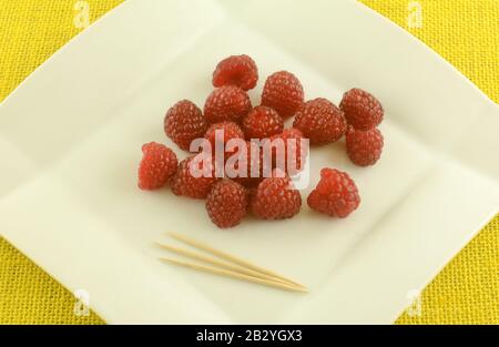 Fresh raw red raspberries on white snack plate with toothpicks Stock Photo