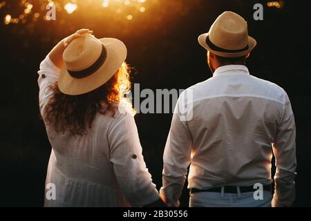 Caucasian man and his overweight charming wife wearing a white dress and hat are posing against the sunset Stock Photo