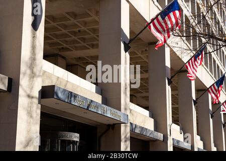 Sign above entrance to the J. Edgar Hoover FBI Building, American flags seen waving in the background. Stock Photo