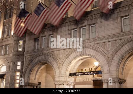 Trump International Hotel sign in-focus at the main entrance on Pennsylvania Ave in Washington, D.C. with American flags waving above at night. Stock Photo
