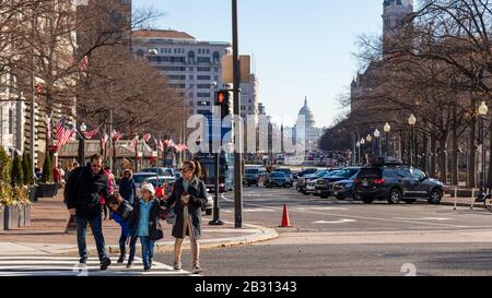 Family crosses 15th Street at Pennsylvania Avenue on a sunny day in DC, the US Capitol Building can be seen in the distance.