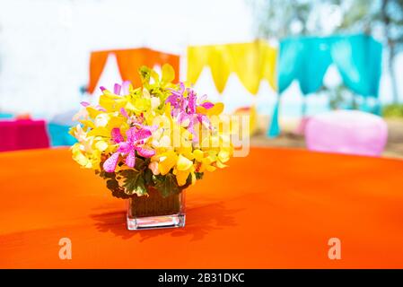 colorful beautiful orchid bouquet decor in glass vase setup on wooden dinner table in India wedding venue reception. Stock Photo