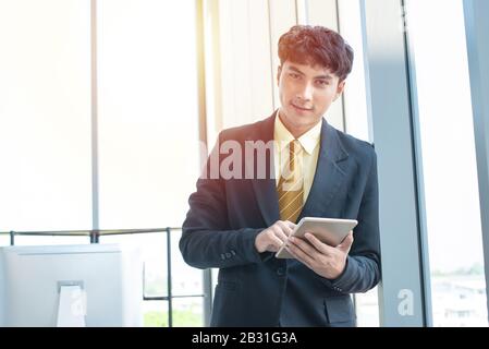 Young asian businessman sitting and working on desk and using digital tablet connecting internet and documents at office, employee or company ceo usin Stock Photo