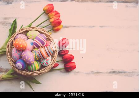 Colorful eggs painted decoration in wood basket on pastel wood backgrounds with tulip flowers for April Easter day with copy space Stock Photo