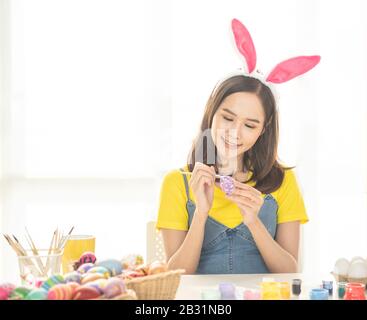 Beautiful young asian woman painting easter eggs on table with decorated eggs for celebrate April Easter day with copy space. Stock Photo