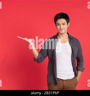 smiling casual young asian man or student college university welcoming invite hand isolated on red studio background Stock Photo
