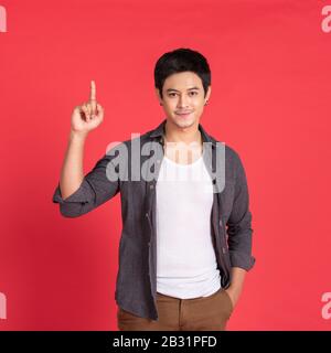 Attractive young handsome asian man in casual t-shirt pointing up with his finger isolated on red background in studio. Stock Photo