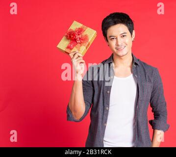Happy handsome young asian man giving Christmas gift isolated on red background in studio shot. Stock Photo