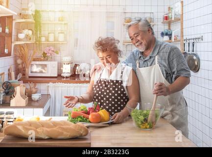Senior couple having fun in kitchen with healthy food - Retired people cooking meal at home with man and woman preparing lunch with bio vegetables Stock Photo
