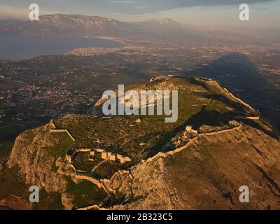 AERIAL VIEW. Ancient city of Corinth overlooking the Gulf of Corinth and the new city of Corinth at sunset. Peloponnese, Greece. Stock Photo