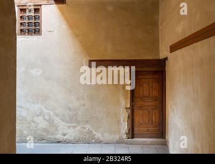 Wooden aged decorated door and small window covered with wooden grid on grunge stone wall Stock Photo