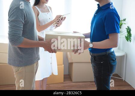 Delivery service worker in uniform delivering parcels to happy asian couple. Woman with tablet signing proof document.shopping online and home deliver Stock Photo