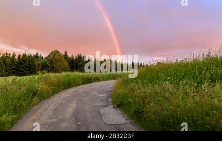 Rainbow over the summer field and road after the evening storm, sunset in countryside with beautiful sky Stock Photo