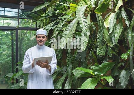 Arab business asian man using tablet,standing in green cafe wear muslim dress ,freelance business concept. Stock Photo