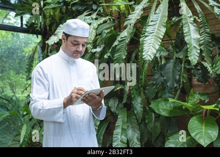 Pakistani business asian man using tablet,standing in green cafe wear muslim dress ,freelance business concept. Stock Photo