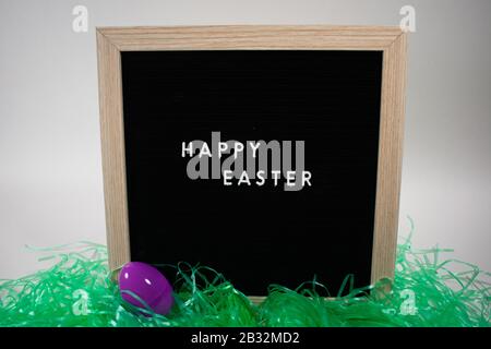 A Black Happy Easter Sign With White Letters, Easter Grass, and Easter Eggs Stock Photo