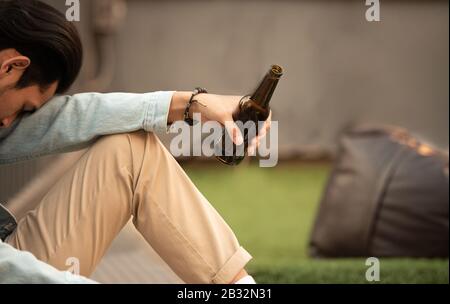 Addiction hungover drunk man hold bottle of beer in hand sit and inactive sleep.Unemployed young asian man suffering from financial problem hopeless Stock Photo