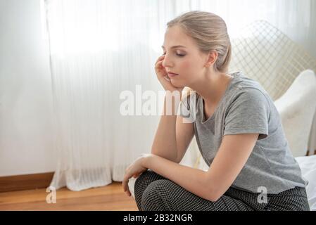 Portrait of sad upset worry and depressed young caucasian woman sit on bed in home with sorrow,hopeless,unhappy in trouble emotion. Stock Photo