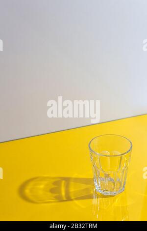 Empty glass with interesting strong hard shadows on yellow background. Play of light. Diagonal lines in frame. Vertical format. Stock Photo