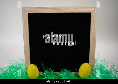 A Black Happy Easter Sign With White Letters, Easter Grass, and Easter Eggs Stock Photo