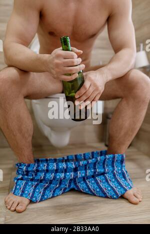 Hangover man with bottle of wine sitting on toilet