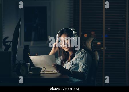 Portrait of Asian Businesswoman sitting and working hard with happiness action on the table with front of computer desktop in workplace at late time, Stock Photo