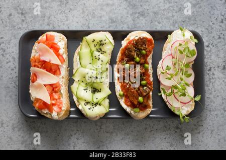 Sandwiches on ciabatta toast with fresh vegetables, radishes, tomatoes, cucumbers and microgreens on gray background. View from above. Stock Photo