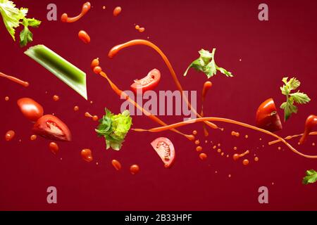 Splashes of tomato juice with celery and tomato slices on a red background. Stock Photo