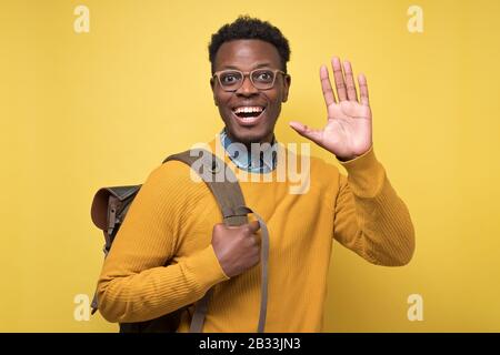 Well hior good bye concept. Young african american welcoming student man toothy smiling and showing five fingers at camera. Studio shot on yellow wall Stock Photo