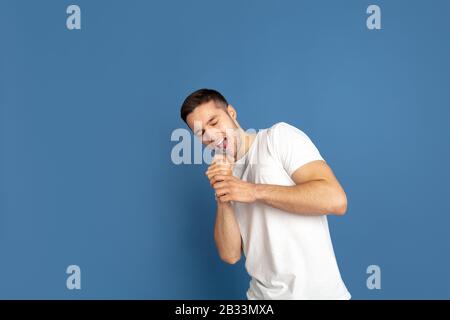 Singing like celebrities, stars. Caucasian young man's portrait on blue studio background. Beautiful male model in casual style, pastel colors. Concept of human emotions, facial expression, sales, ad. Stock Photo