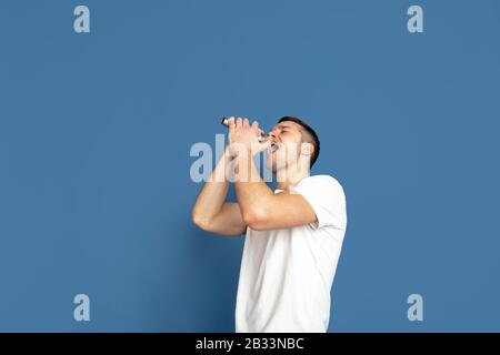 Singing like celebrities, stars. Caucasian young man's portrait on blue studio background. Beautiful male model in casual style, pastel colors. Concept of human emotions, facial expression, sales, ad. Stock Photo