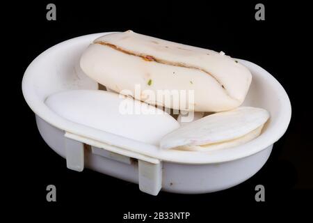 Old rustic dry cracked white soaps slices  in plastic broken dishe. Isolated on black macro Stock Photo