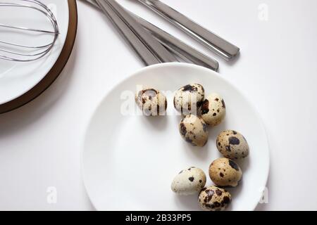 Overhead view of Quail Eggs on a White Plate on a table with Kitchenware. Easter Holiday Table Setting. Stock Photo